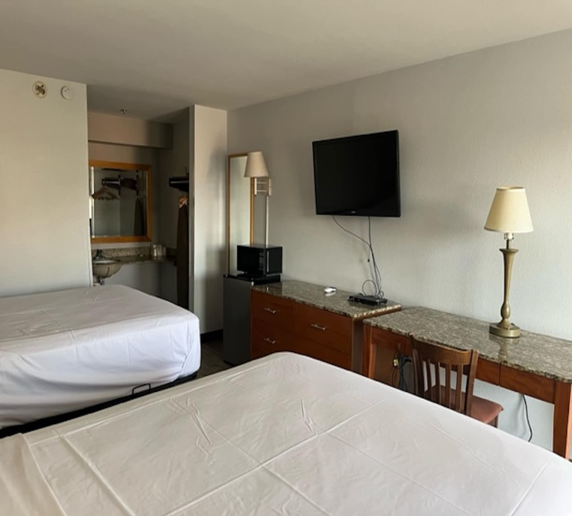 Habitación de hotel con dos camas, un escritorio, un televisor de pantalla plana, un espejo y una lámpara.