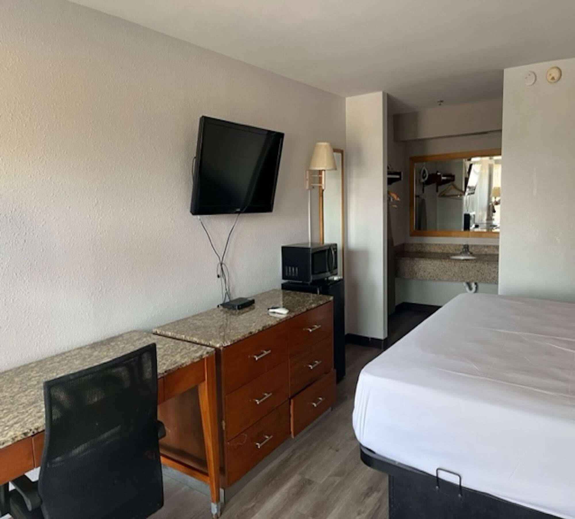 A hotel room with a bed, a desk with a television, a lamp, and a mirror.