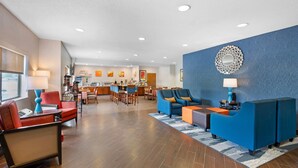 Een moderne hotel lobby met een receptiebalie, een eetgedeelte en zitplaatsen met blauwe en rode stoelen.