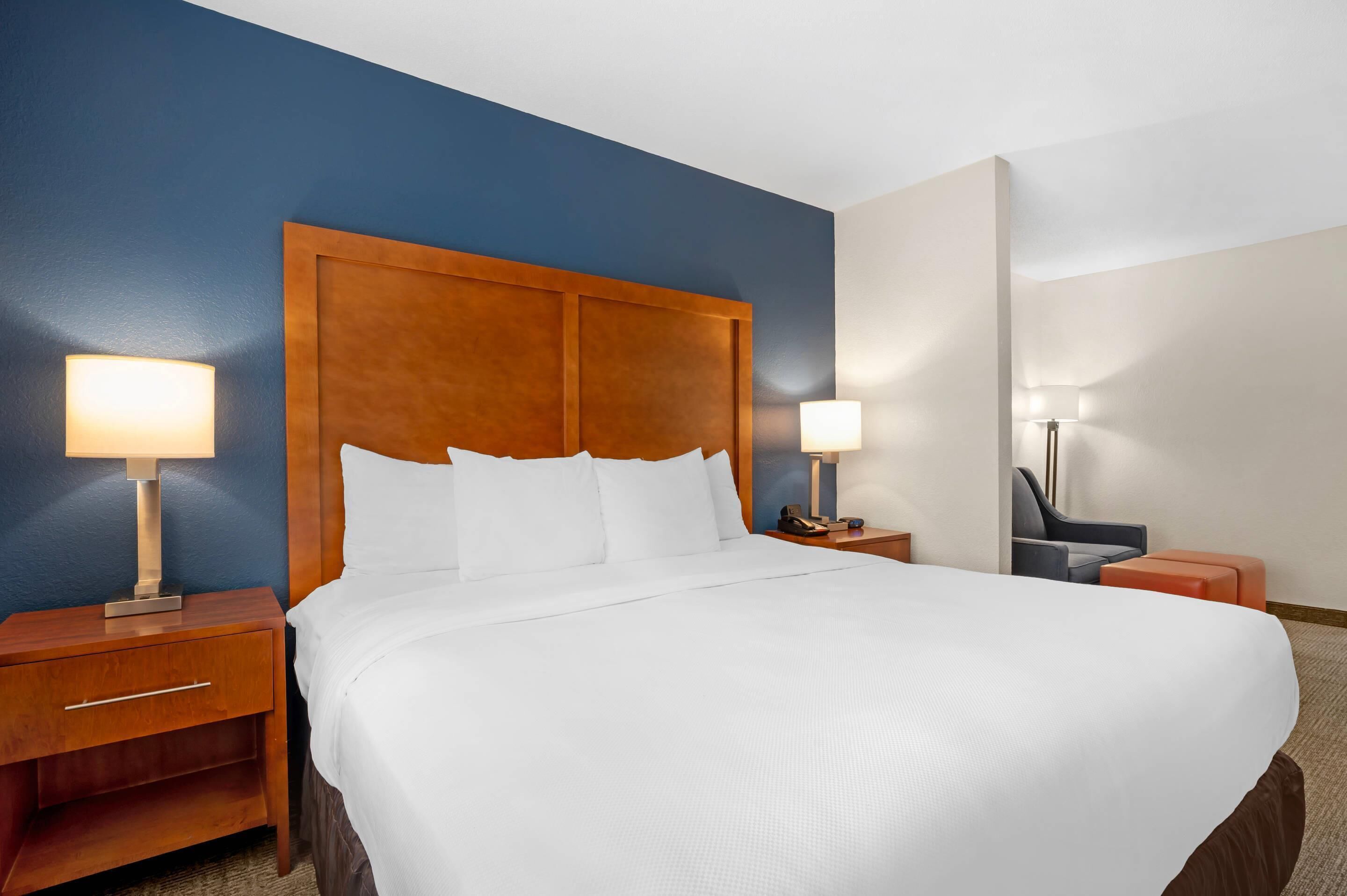 A hotel room with a large bed, wooden headboard, two bedside tables with lamps, and a chair.