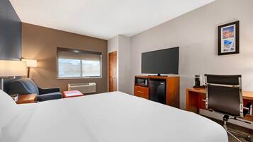 Quarto de hotel com uma cama grande, uma escrivaninha com computador, uma televisão e uma cadeira.
