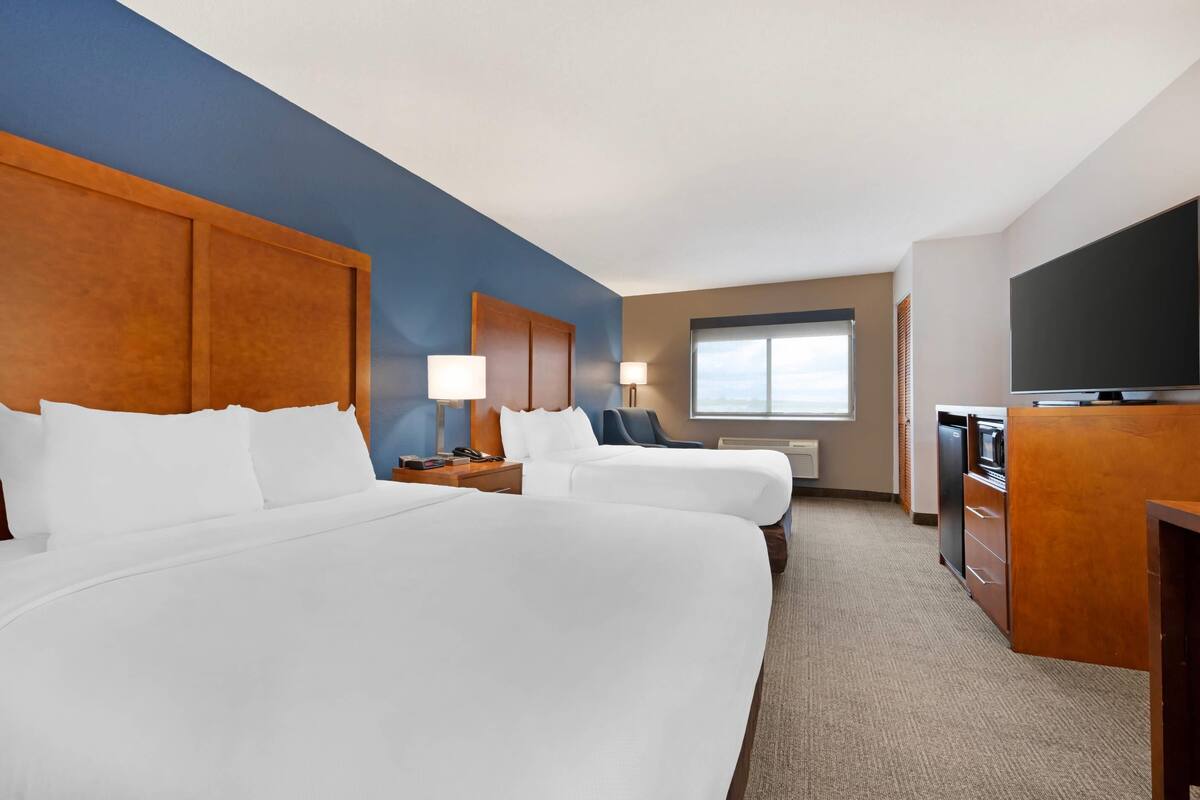 A hotel room with two beds, a TV, a desk, and a window.