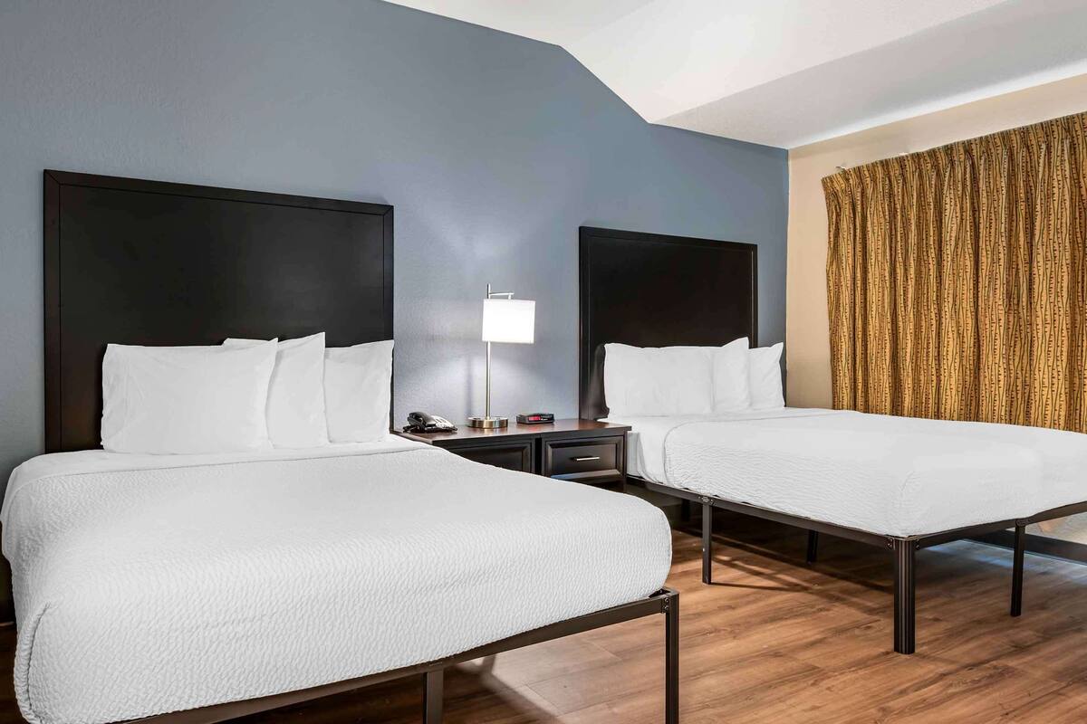A hotel room with two single beds, a nightstand with a lamp, and a curtain on the window.