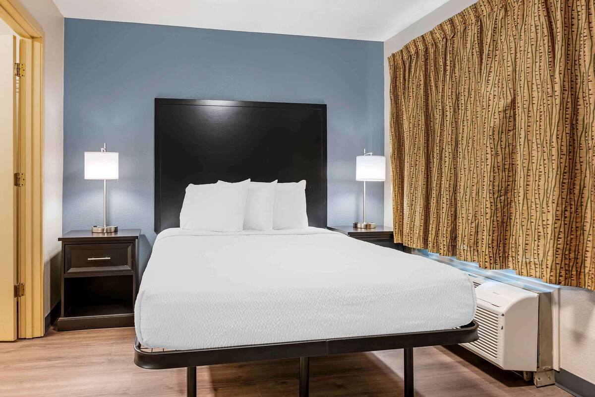 A neatly made bed with a dark headboard, two bedside tables with lamps, and a patterned curtain.