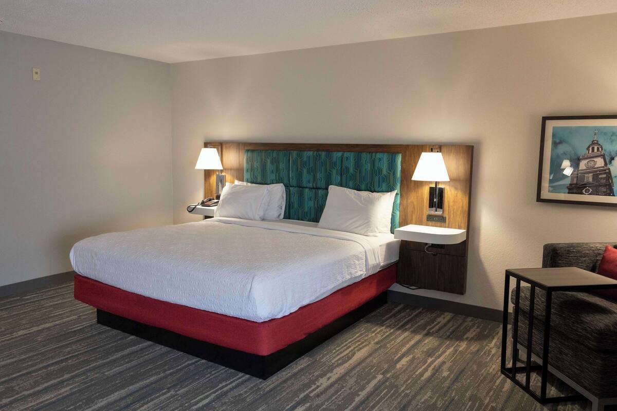 A hotel room with a large bed, two bedside tables with lamps, a small table, and a framed picture on the wall.