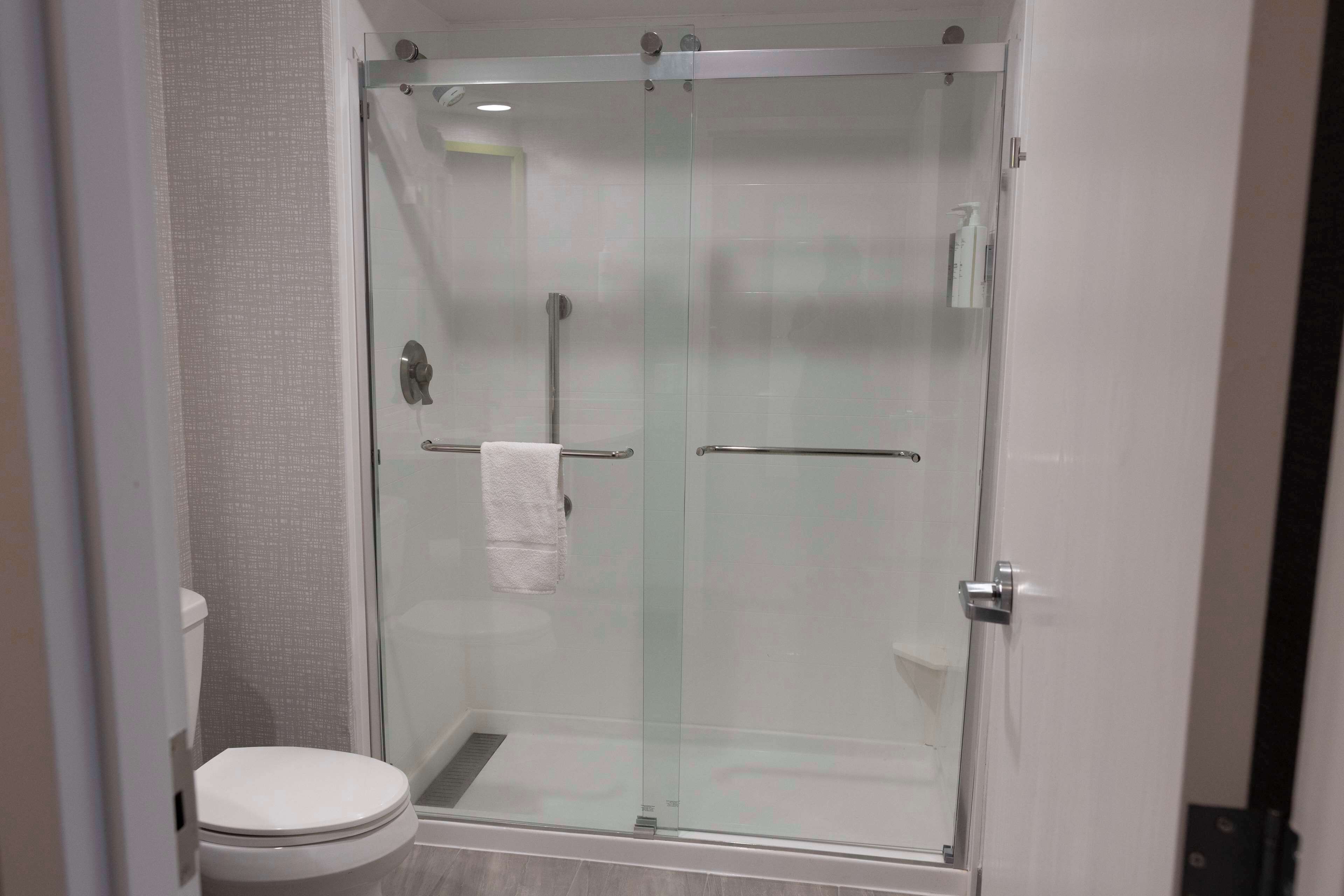 A glass-enclosed shower stall with a white toilet and towel rack.