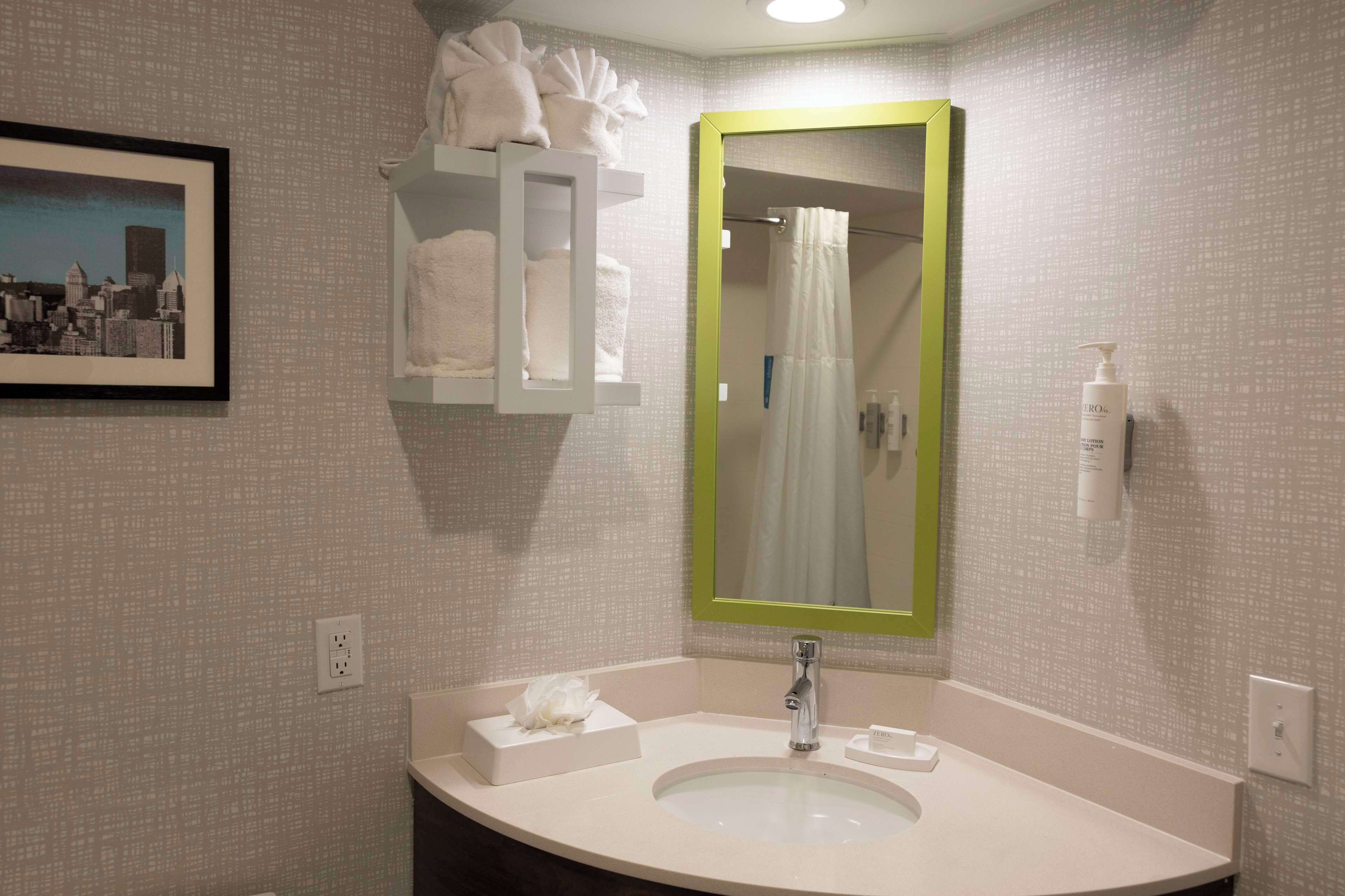 A bathroom with a white sink, a mirror with a green frame, a towel rack with towels, and a framed picture on the wall.