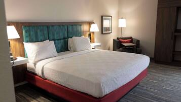 Habitación de hotel con una cama grande, dos lámparas de noche, una silla y un armario de madera.