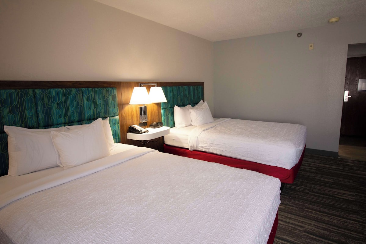 A hotel room with two beds, a nightstand with a lamp, and a wooden headboard.