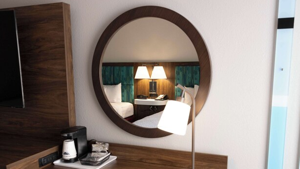 A hotel room with a round mirror, a bedside lamp, a coffee maker, and a small table with a tray. - Hampton Inn Kent/Akron Area (Kent)