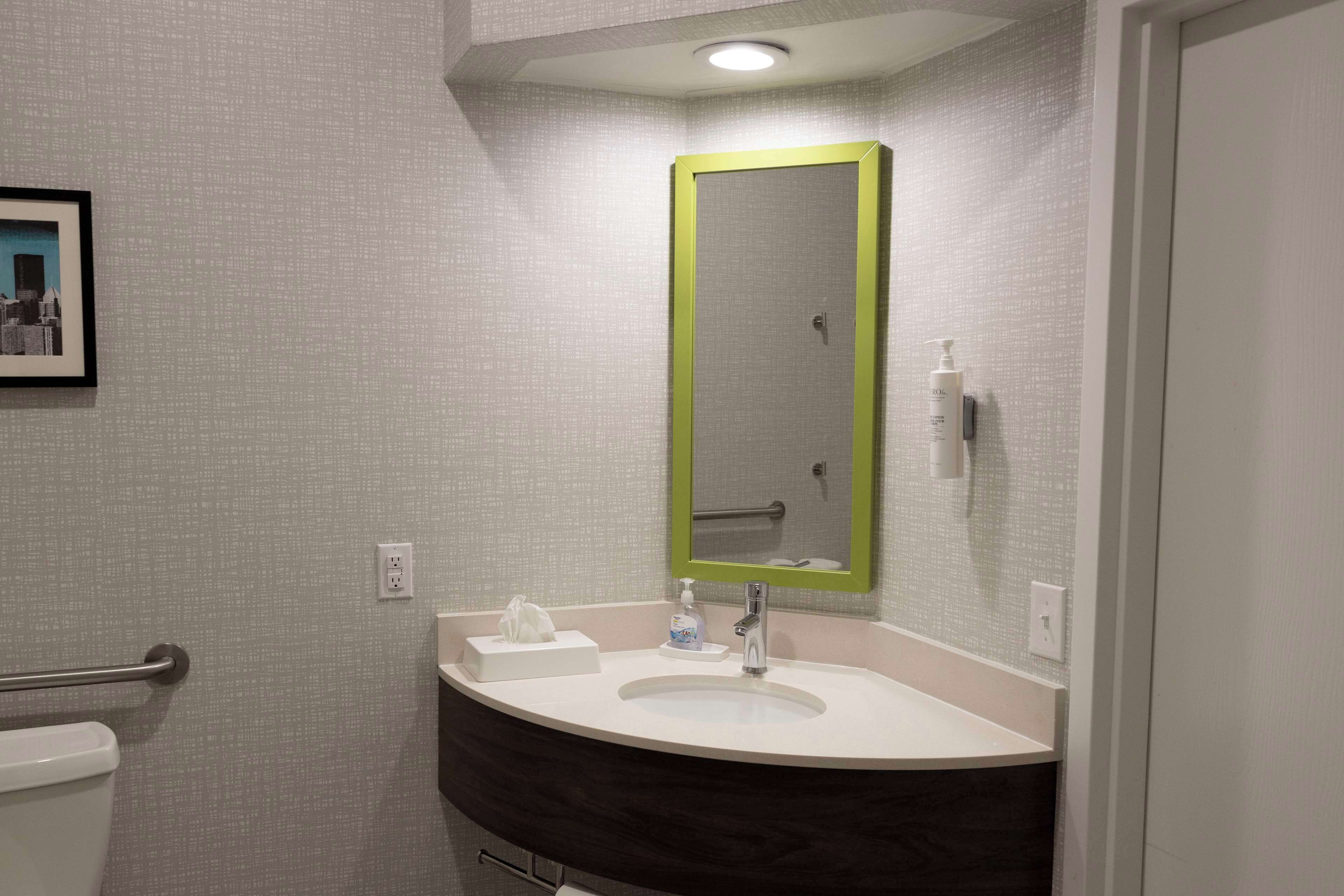 Een badkamer met een witte wastafel, een spiegel met groene lijst en een zeepdispenser.