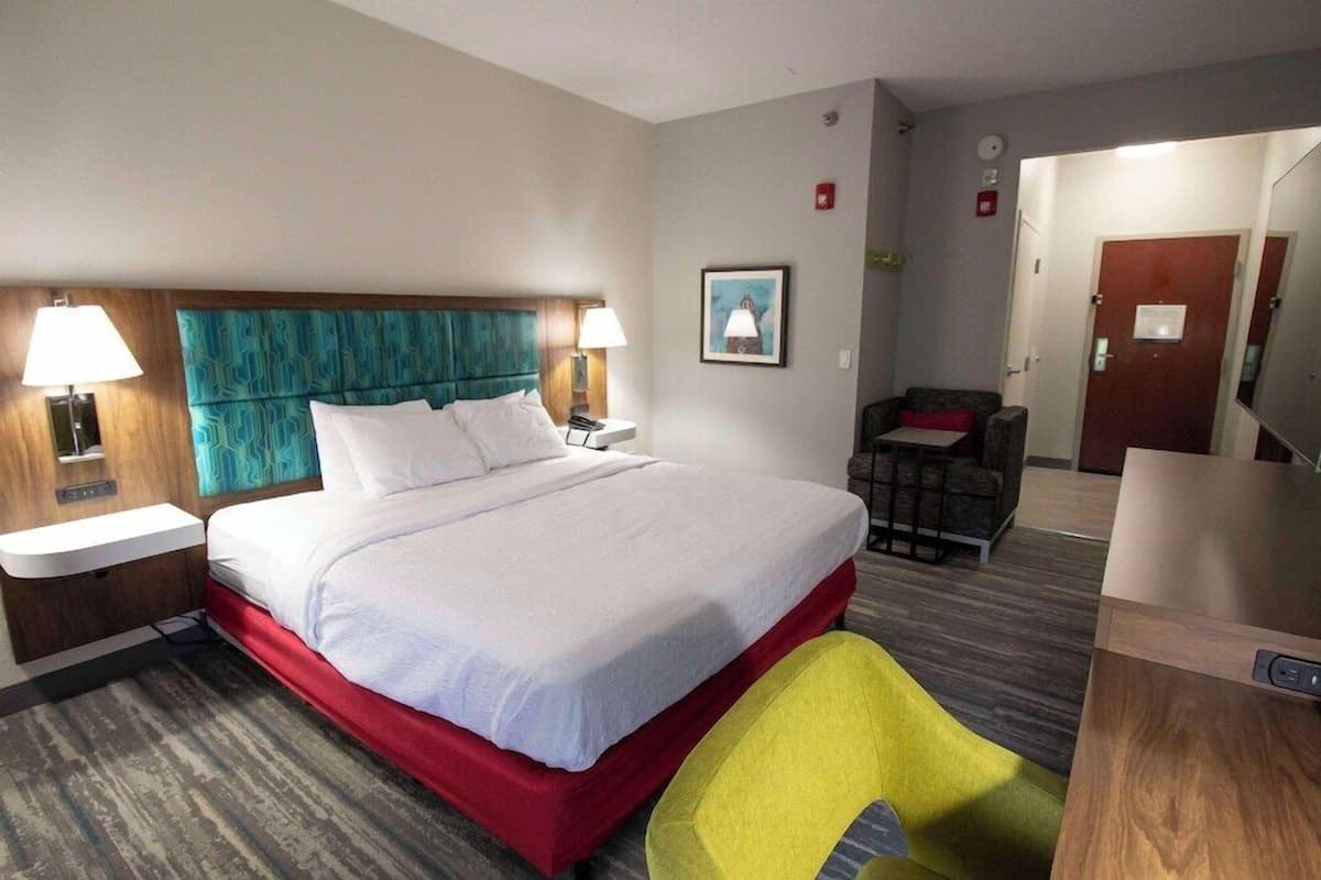 A hotel room with a bed, bedside tables, a chair, a desk, and a door.