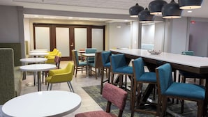 A modern dining area with round tables and chairs, a long communal table, and pendant lighting. - Hampton Inn Kent/Akron Area (Kent)