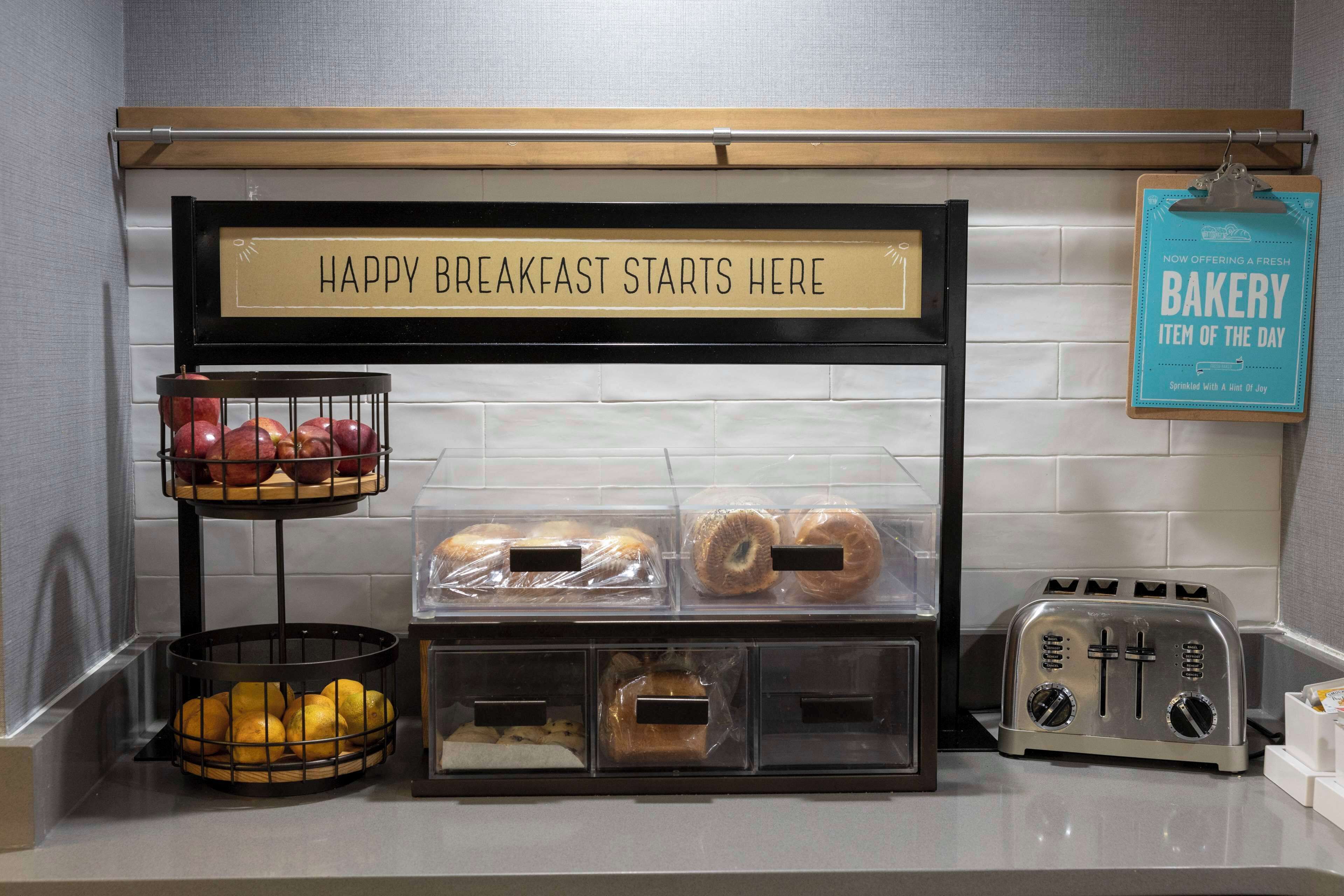 Una estación de desayuno con un letrero que dice “HAPPY BREAKFAST STARTS HERE” y un letrero que indica un producto de panadería diario.