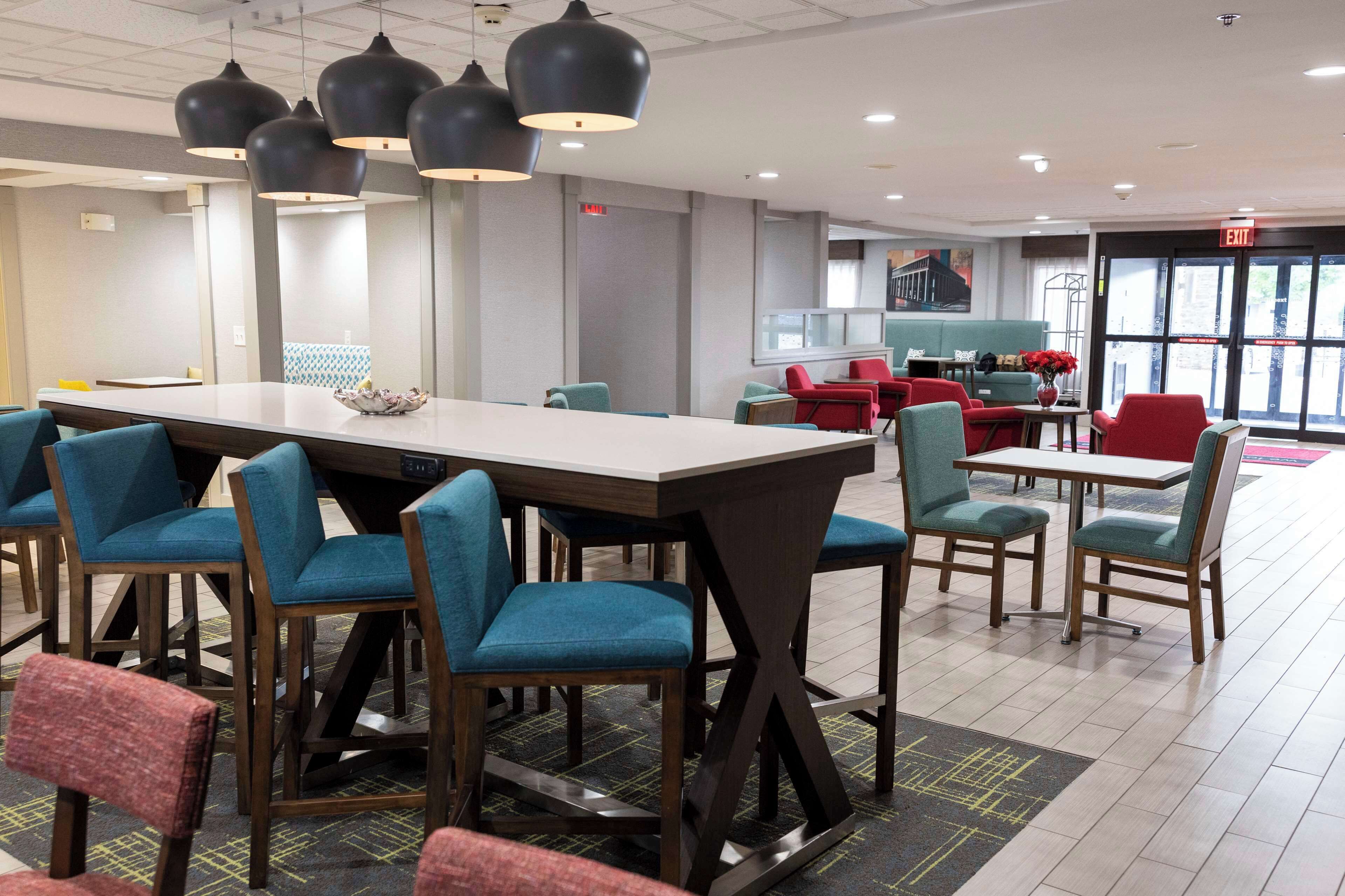 A modern hotel lobby with a long reception desk, blue and red seating, and pendant lighting.