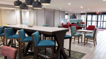 A modern hotel lobby with a long reception desk, blue and red seating, and pendant lighting.