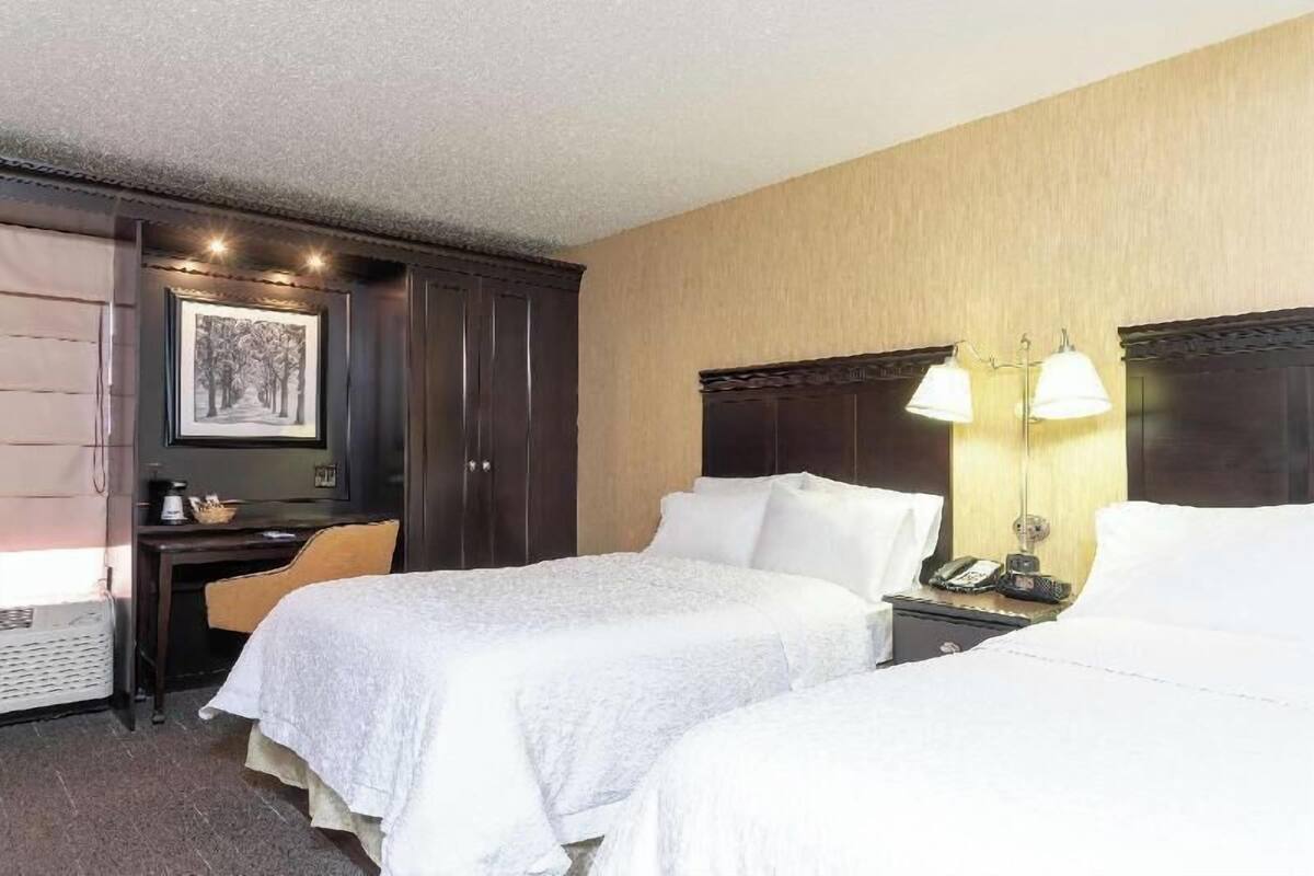 A hotel room with two beds, a desk with a chair, a wardrobe, and a framed picture on the wall.