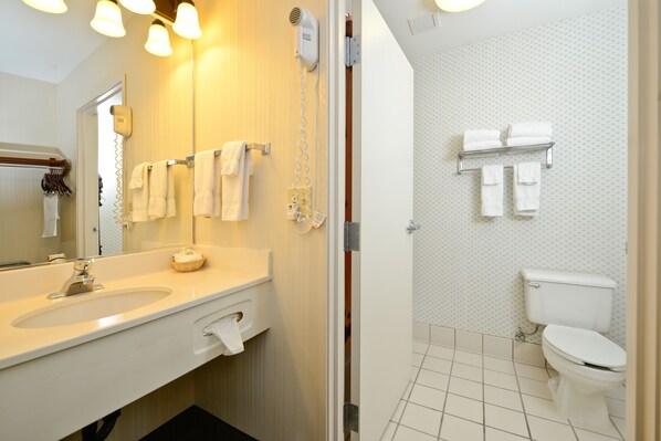 Un baño con lavamanos, espejo, toallero y retrete.