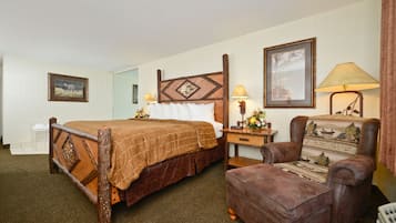 A hotel room with a wooden bed, a brown armchair, a nightstand with a lamp, and a framed picture on the wall.