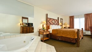 A hotel room with a large bathtub, a bed with a brown bedspread, a wooden nightstand with a lamp, and a mirror above the dresser. - ClubHouse Inn West Yellowstone (West Yellowstone)