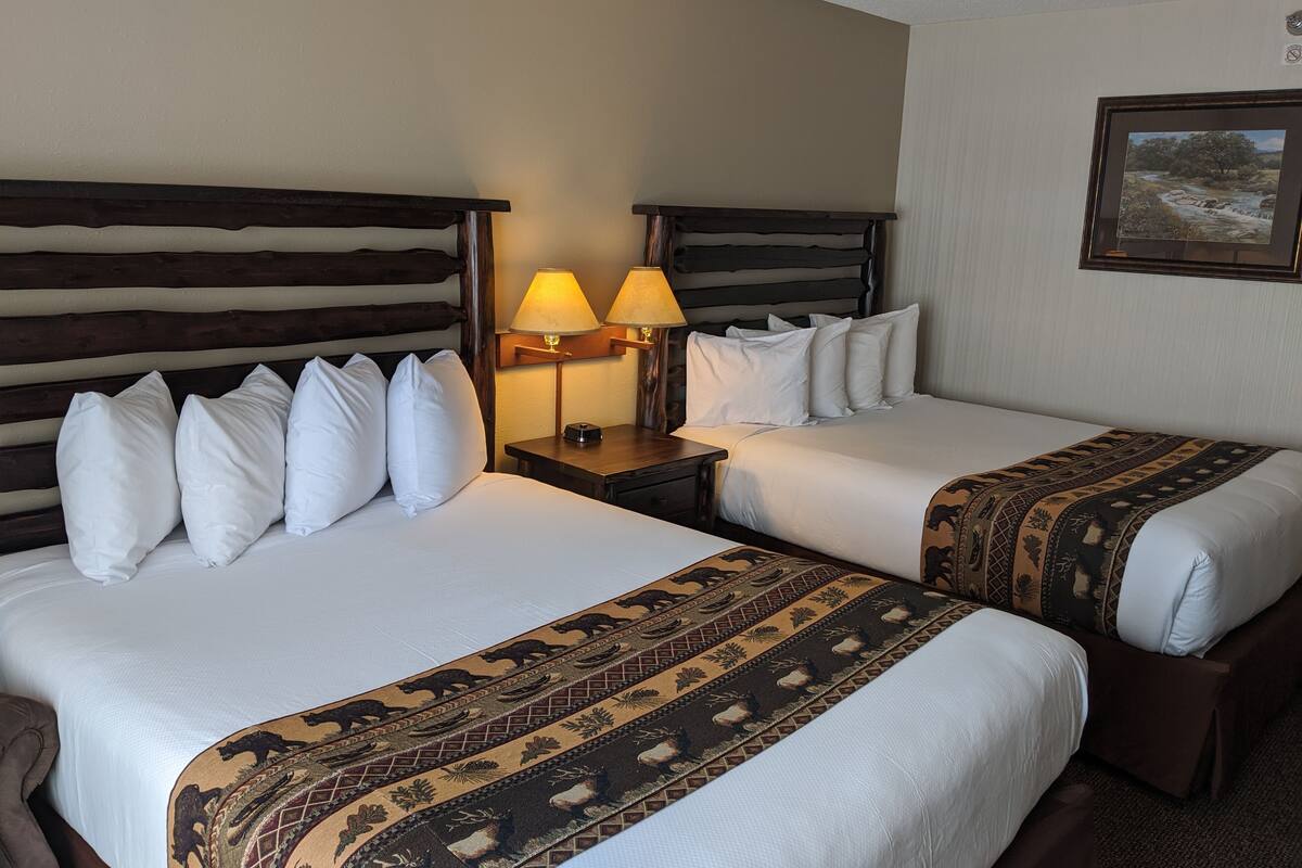Une chambre d’hôtel avec deux lits, chacun agrémenté de draps blancs et d’un plaid à motifs. Il y a deux tables de chevet avec des lampes.