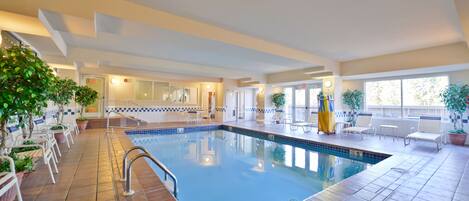 Una piscina interior con suelo de baldosas, una escalera de piscina y sillones de descanso alrededor del área de la piscina.