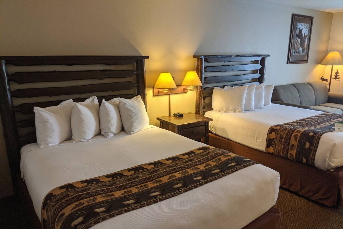 Une chambre d’hôtel avec deux lits, chacun doté d’une tête de lit en bois et de linge de lit blanc. On y trouve deux lampes de chevet avec des abat-jour jaunes, ainsi qu’un tableau encadré accroché au mur.