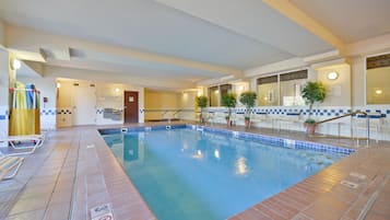 Una piscina interior con paredes de azulejos y agua de color azul cristalino. Se observan sillas de descanso y un cartel que indica que no hay socorrista de servicio.