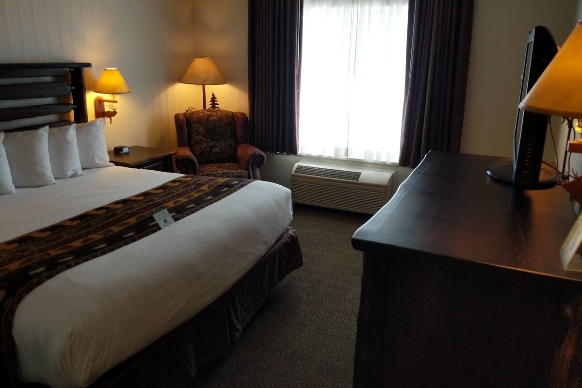 Une chambre d’hôtel avec un grand lit, un bureau, une chaise, une lampe et une fenêtre avec des rideaux.