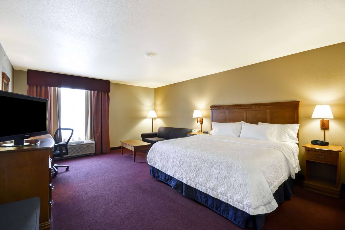 A hotel room with a large bed, two bedside lamps, a desk with a television, and a chair.