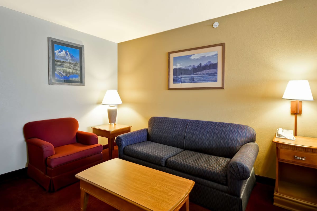 A hotel room with a red armchair, a blue sofa, a wooden table, two lamps, and two framed pictures on the walls.