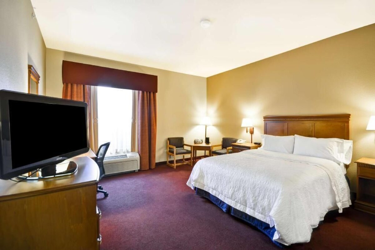 A hotel room with a bed, a desk with a computer, a television, and a window with curtains.