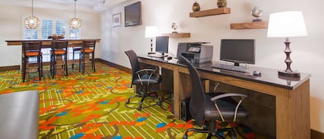 Une chambre d’hôtel équipée d’un bureau, de deux chaises, d’un ordinateur, d’une télévision et d’une moquette aux couleurs vives.