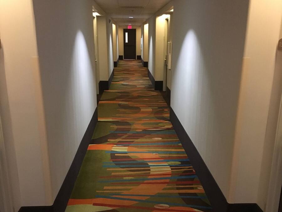 Un pasillo de hotel con piso alfombrado, paredes blancas y puertas a ambos lados.