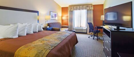 A hotel room with a large bed, a desk with a television, a chair, a desk lamp, and a window with curtains.