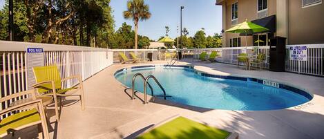 A swimming pool with a white fence, lounge chairs, and a sign indicating no lifeguard on duty.
