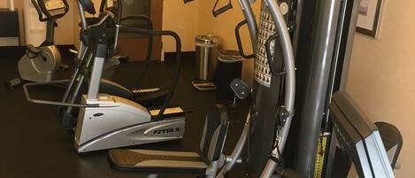 A gym with various exercise machines, a water dispenser, and a trash can.