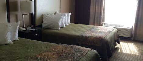 A hotel room with two beds, a nightstand, a lamp, and a window with curtains.