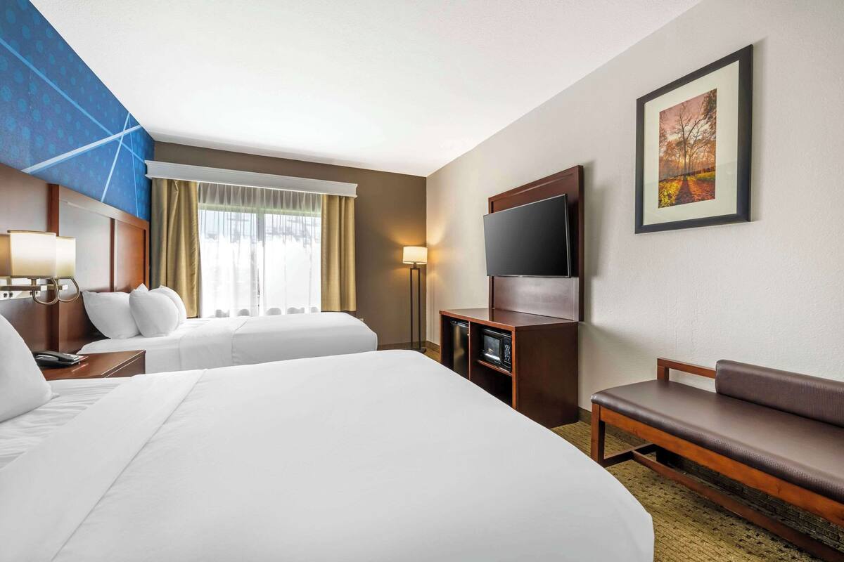 Ein Hotelzimmer mit zwei Betten, einem Fernseher, einem Schreibtisch, einer Lampe und einem Bild an der Wand.