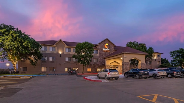 A hotel with a 'Comfort Suites' sign, multiple parking spaces, and a building with a red roof. - Comfort Suites Omaha East-Council Bluffs (Council Bluffs)