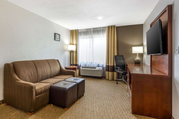 Habitación de hotel con sofá marrón, escritorio de madera, televisor de pantalla plana, unidad de aire acondicionado y lámpara.