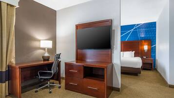 A hotel room with a wooden desk, a chair, a TV, a bed, and a nightstand.