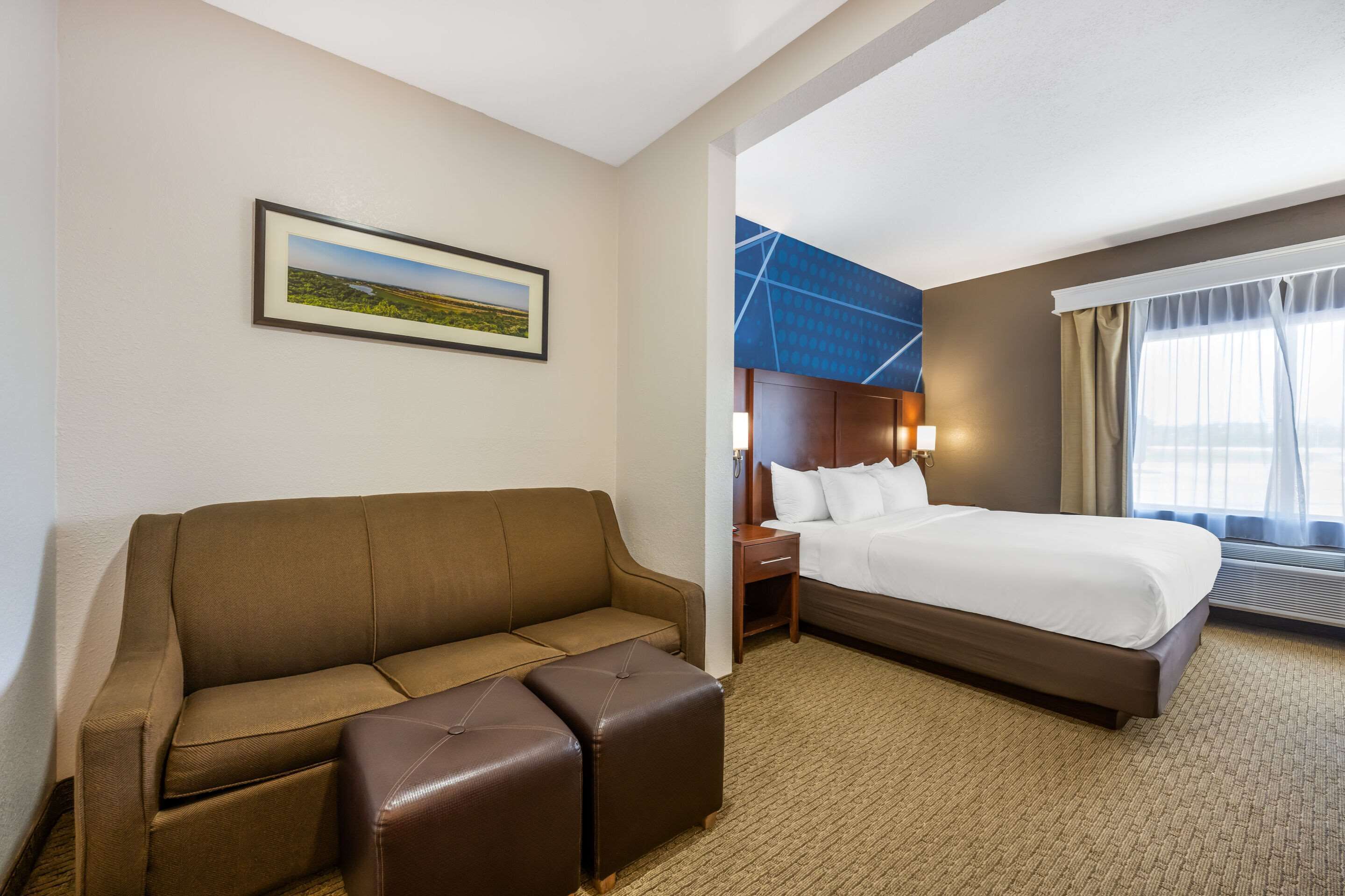 A hotel room with a brown sofa, a bed, a nightstand, and a framed picture on the wall.