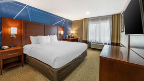 A hotel room with a large bed, a desk, a TV, a nightstand, and a wall-mounted lamp. - Comfort Suites Omaha East-Council Bluffs (Council Bluffs)