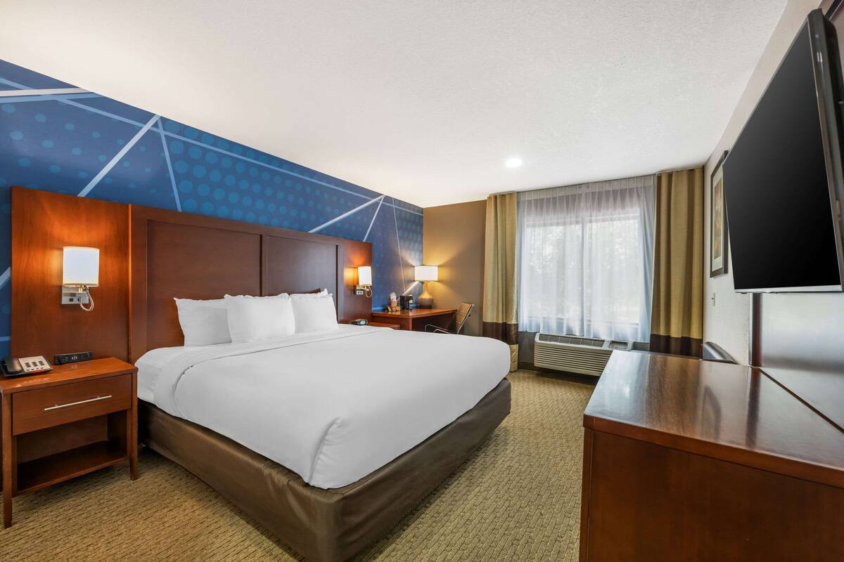 Ein Hotelzimmer mit einem großen Bett, einem Schreibtisch, einem Fernseher, einem Nachttisch und einer Wandleuchte.