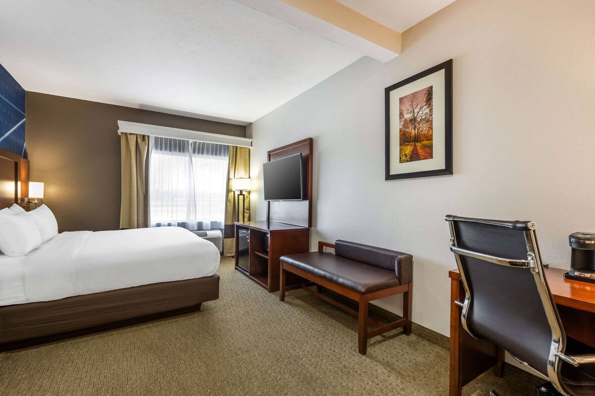 Ein Hotelzimmer mit Bett, Schreibtisch mit Stuhl, Fernseher und einem gerahmten Bild an der Wand.