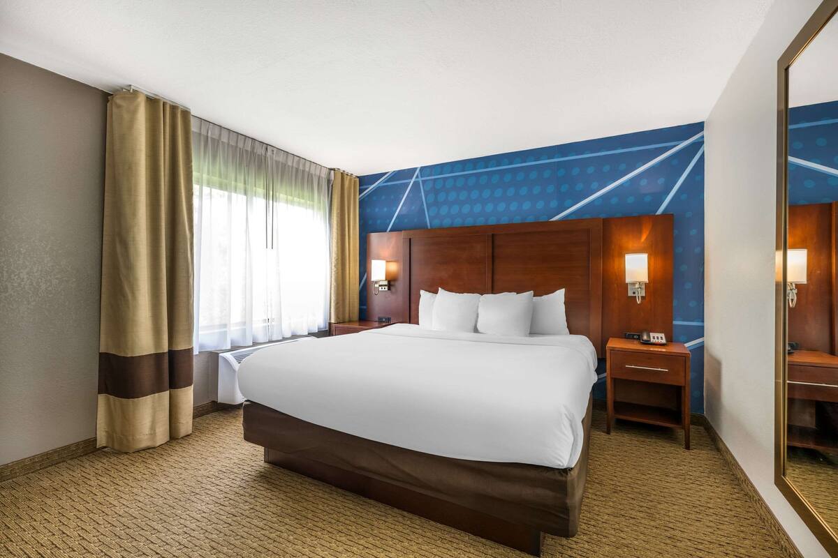 Ein Hotelzimmer mit einem großen Bett, zwei Nachttischen mit Lampen, einem Spiegel und einer Wand mit einem geometrischen Muster.