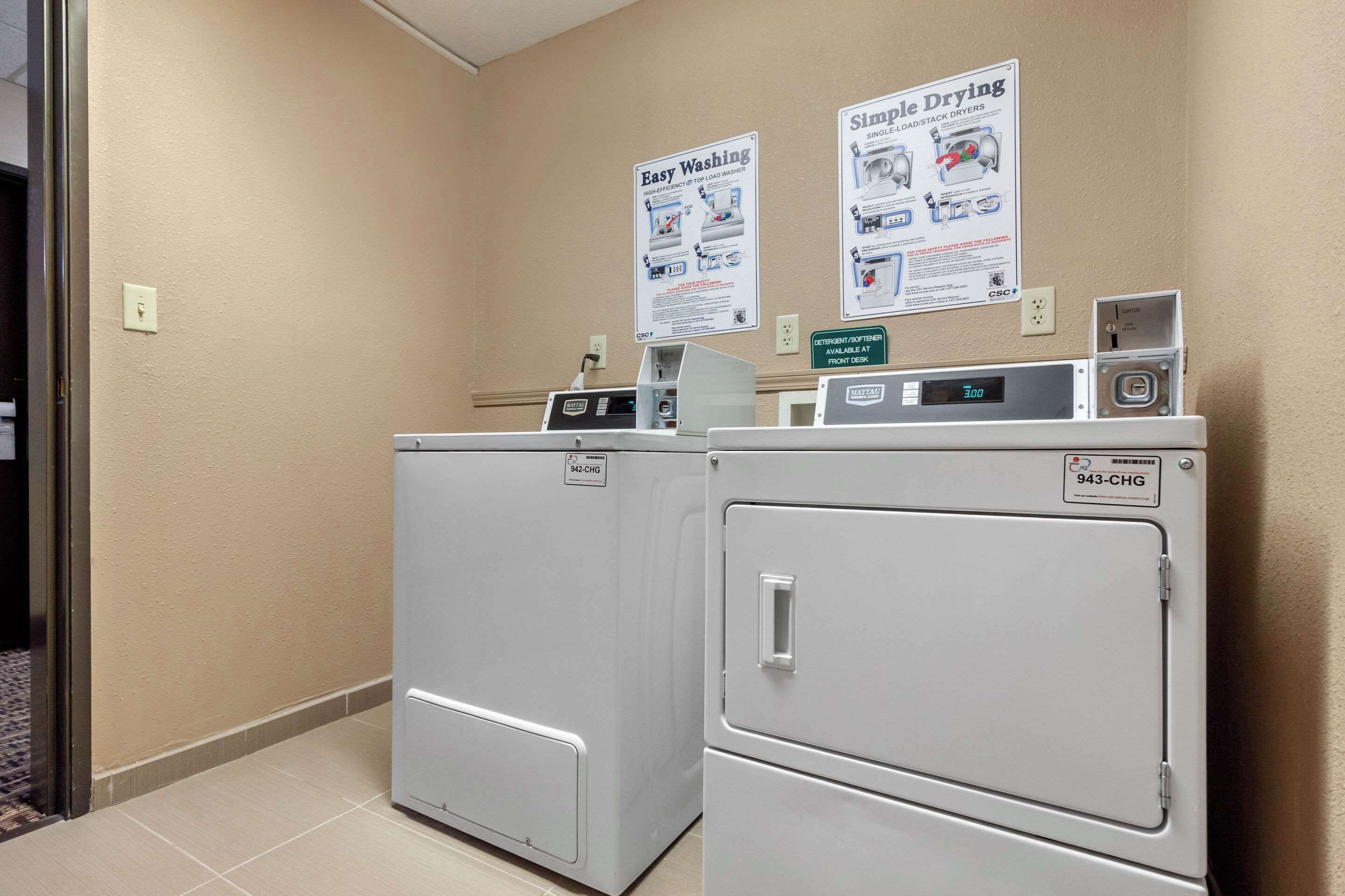 A laundry area with two washers and dryers, a digital display, and informational posters on the wall.