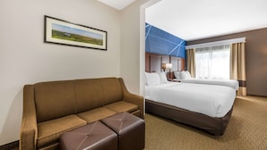 A hotel room with a brown sofa, a large bed, and a framed landscape picture on the wall. - Comfort Suites Omaha East-Council Bluffs (Council Bluffs)