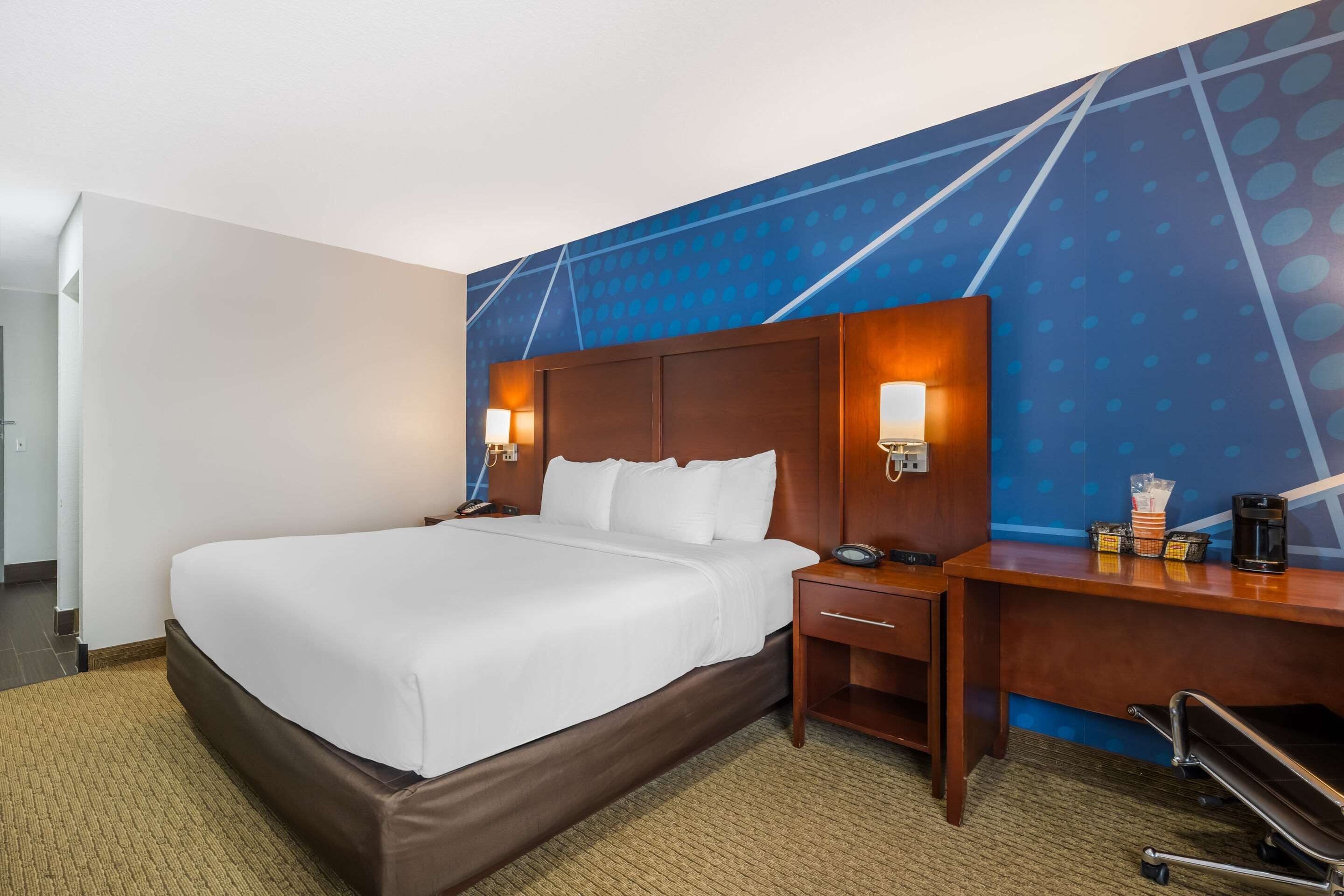 A hotel room with a large bed, a desk with a chair, and a wall with a geometric pattern.
